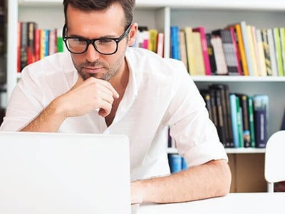 A man sitting at a desk looking at a laptop.