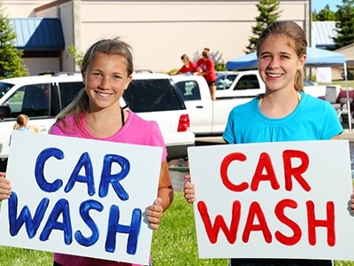 Two girls holding up signs that say car wash.