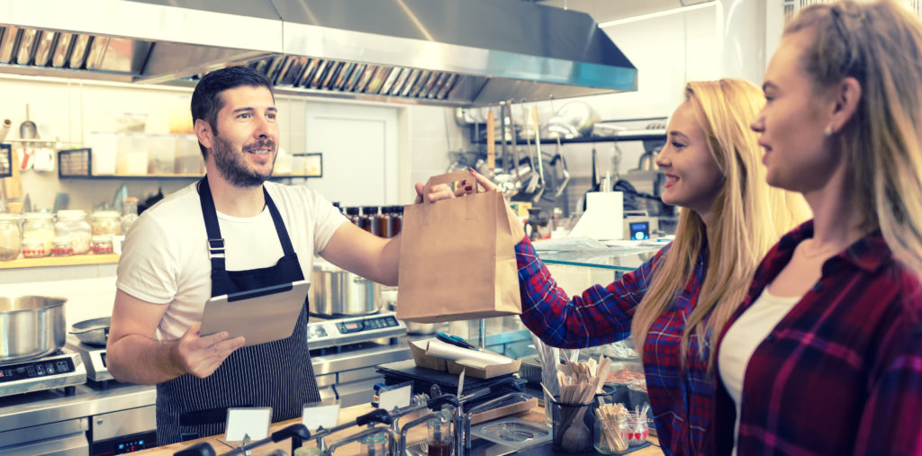 A man is handing a bag to a woman in a restaurant.