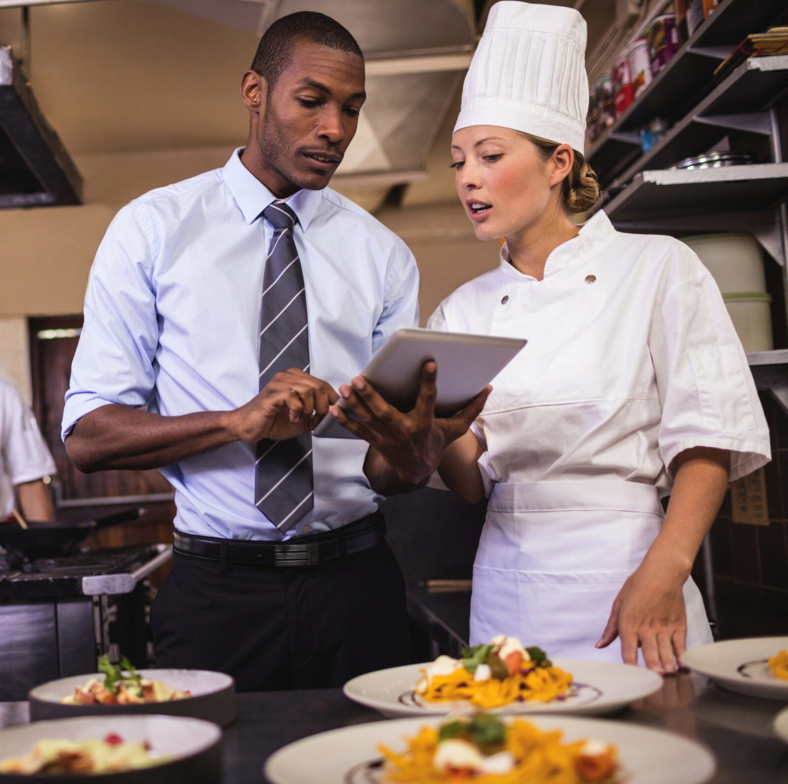 A man and a woman in a kitchen looking at a tablet.