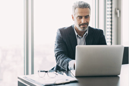 A man in a suit sitting at a desk with a laptop.