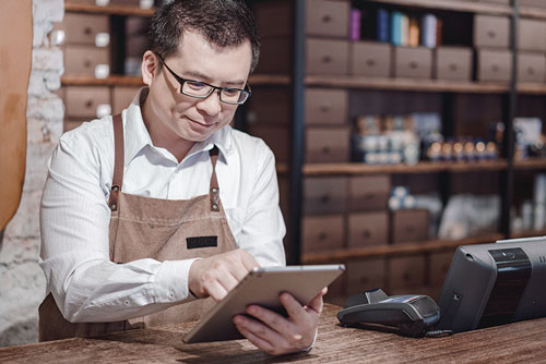 A man in an apron is using a tablet in a store.