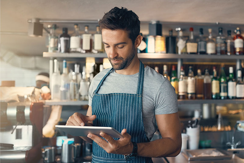A man in an apron is using a tablet in a bar.