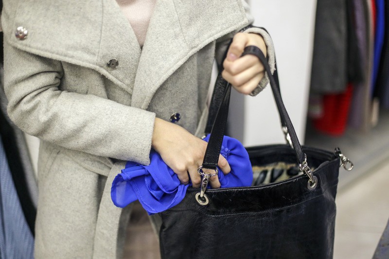 Theft-woman-stealing-clothes A woman holding a purse in a clothing store.