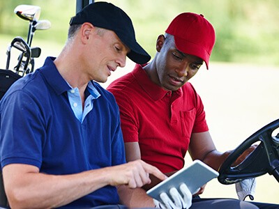 Two men in a golf cart looking at a tablet.