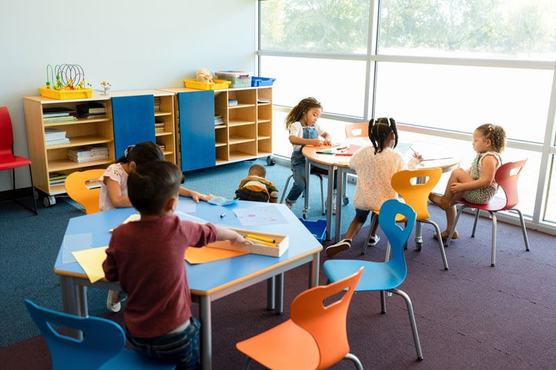 A group of children sitting at tables in a classroom.