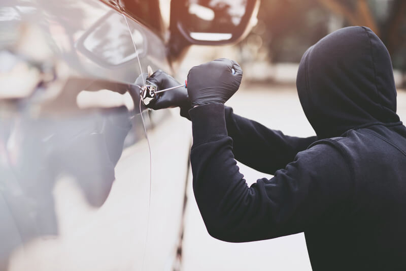 A person in black clothing trying to break into a car with a screwdriver