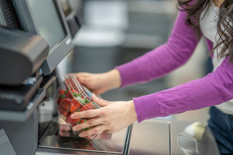 A woman paying for strawberries at a grocery store self checkout