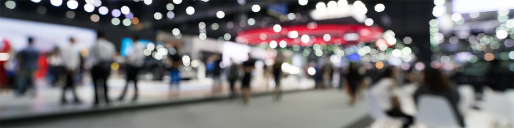 A blurry image of people walking through a trade show.