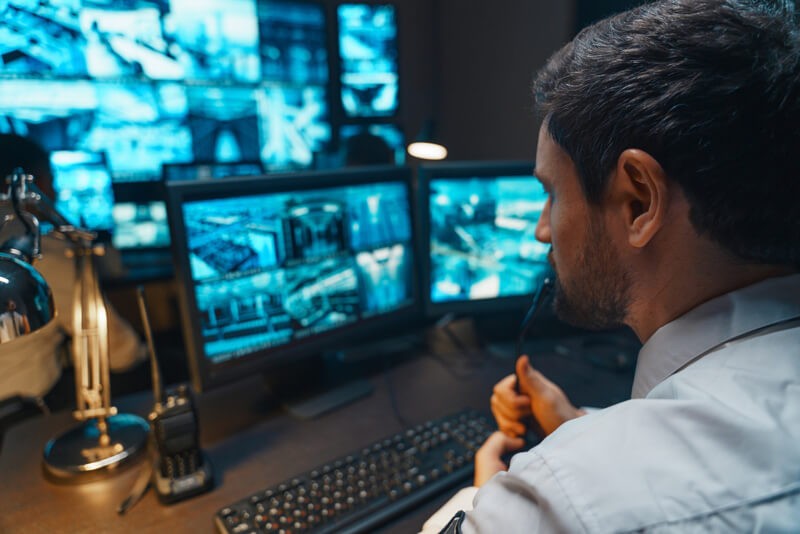 A security guard sitting at a desk viewing multiple monitors and video feeds