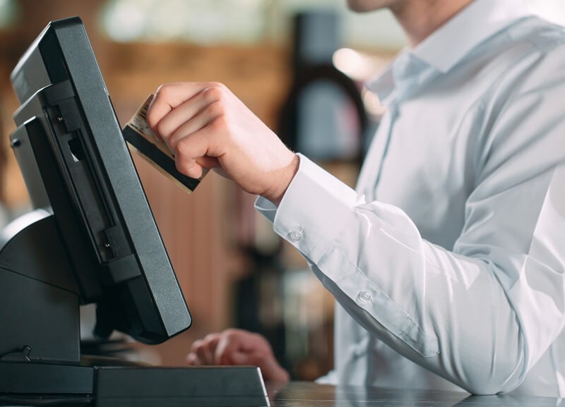 A close up of a employee swiping a credit card through a payment terminal at the register
