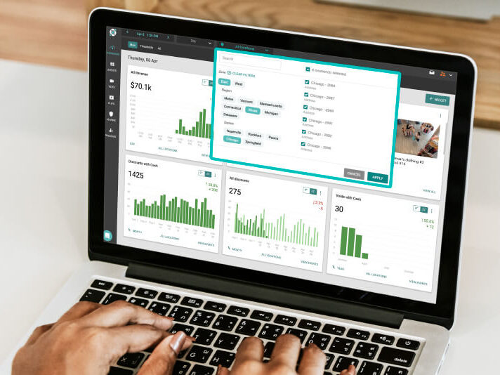 A person uses a laptop displaying data analytics dashboards with various charts, graphs, and a settings window open on the screen.
