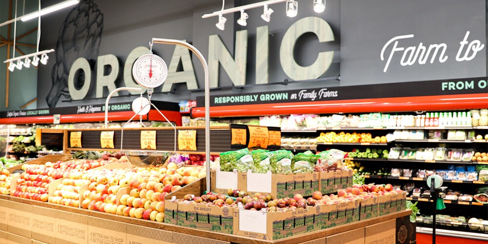 A grocery store with fresh fruit and produce. In the background, a large sign displays the word "organic"