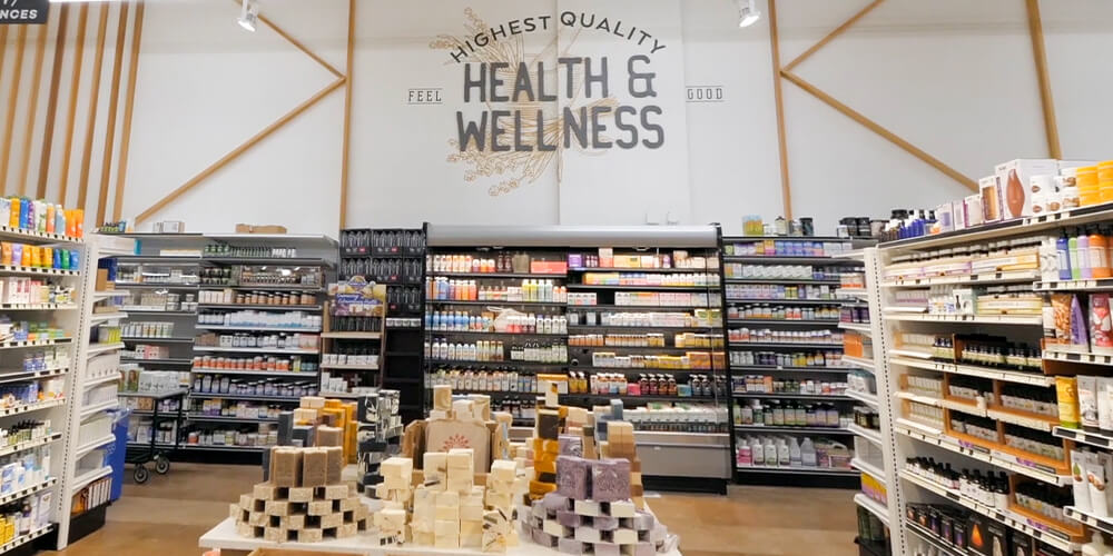 A grocery store aisle. In the background, a large sign that displays "Health & Wellness" is above the aisle