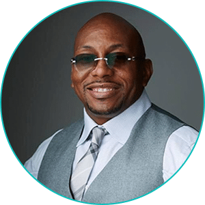 A black man wearing sunglasses and a vest.