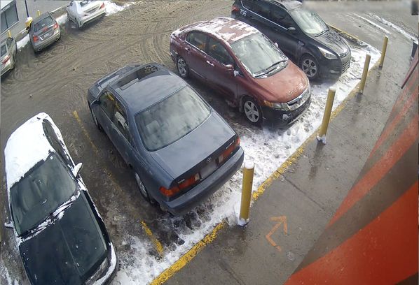 A camera captures several cars parked in a parking lot.