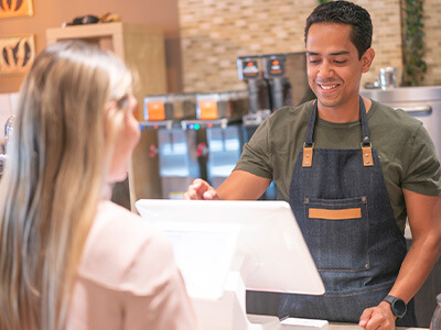 A smiling barista serves a female customer at a coffee shop register.