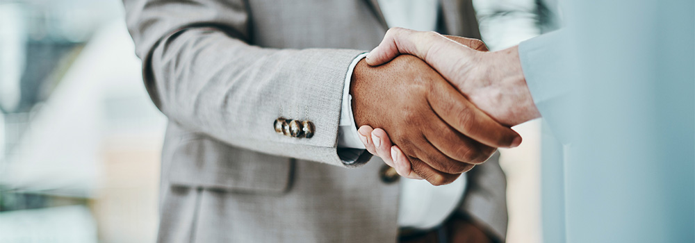 Close-up of two businesspeople shaking hands, focusing on their clasped hands with blurred background.