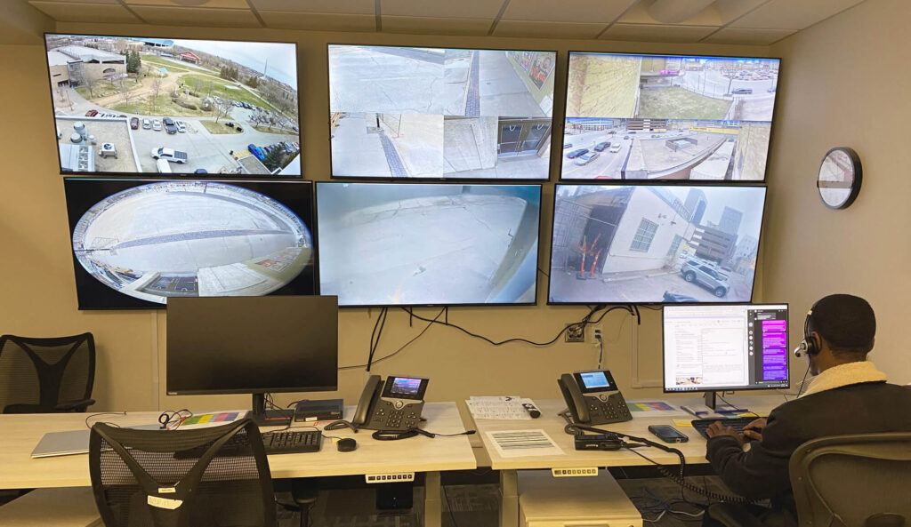 Security personnel monitoring multiple cctv screens showing various outdoor locations in a surveillance control room.