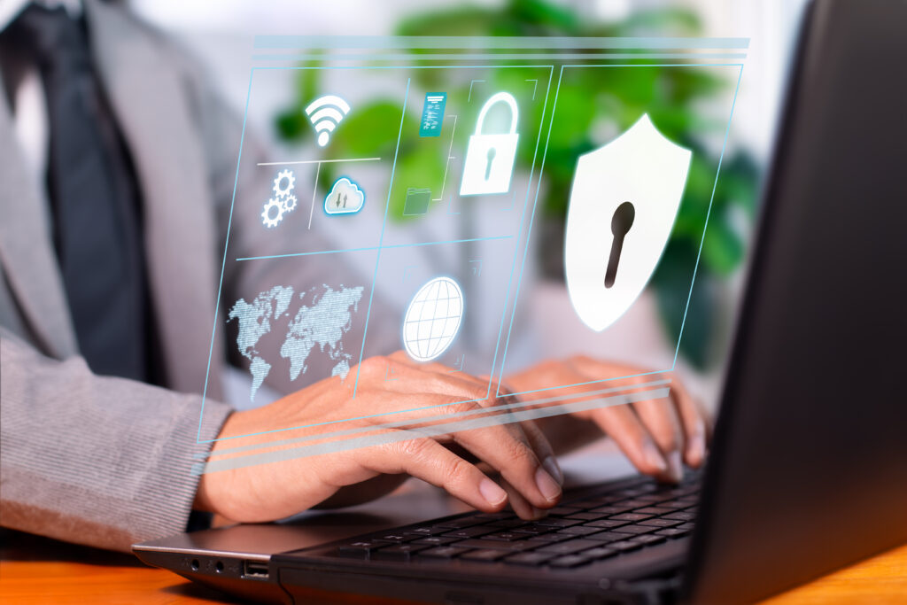 Person working on a laptop with holographic security icons, including a padlock, shield, and Wi-Fi symbol, displayed above the keyboard.