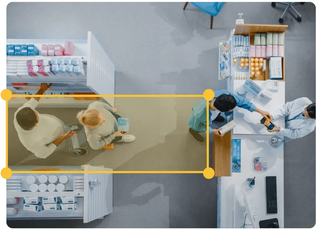 Top view of a pharmacy with two people shopping, a cashier scanning items, and a pharmacist working at the counter.