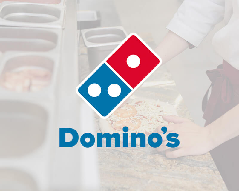 Domino's logo over a blurred background of a person making pizza in a kitchen setting.