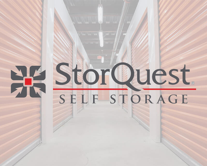 StorQuest Self Storage logo overlaid on an image of a hallway with orange storage unit doors.