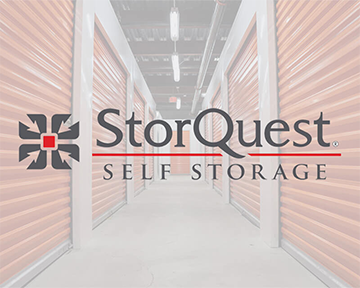 Interior hallway of a storage facility with orange roll-up doors and the StorQuest Self Storage logo overlaid in the center.