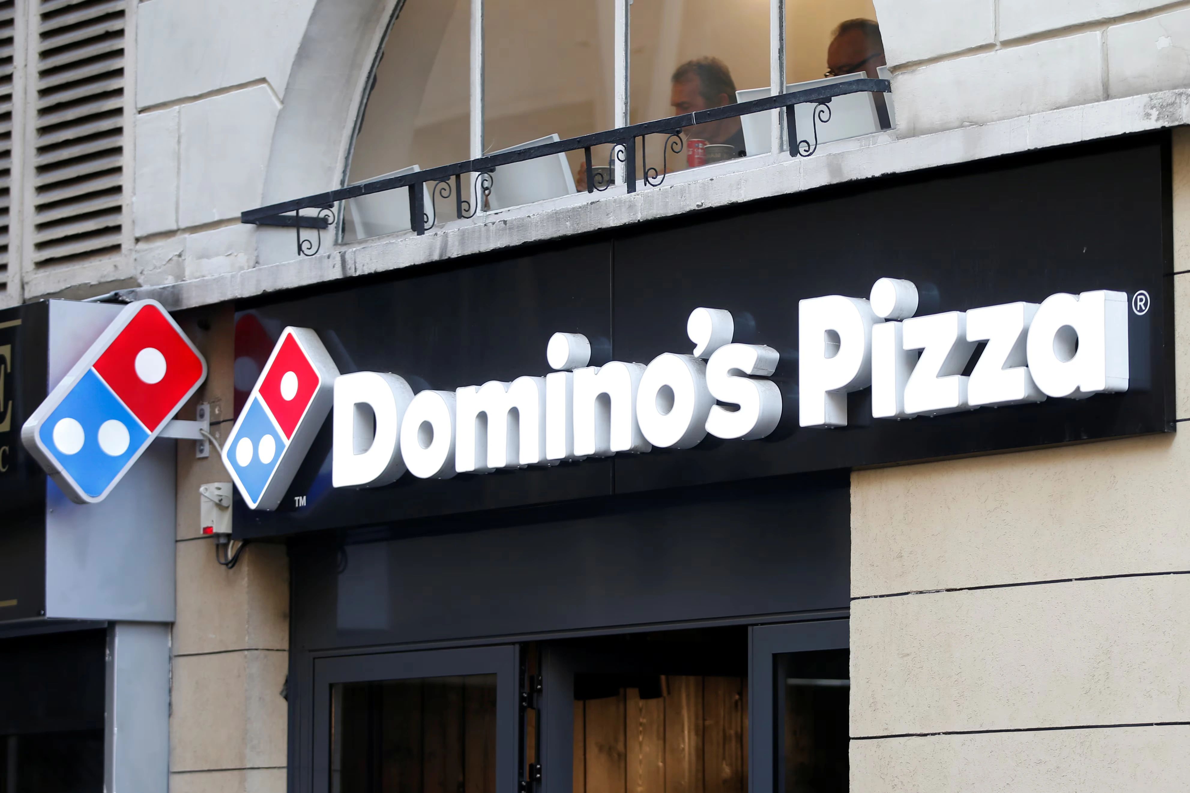 The front of a Domino's Pizza restaurant with a large illuminated sign and the Domino's logo above the entrance.