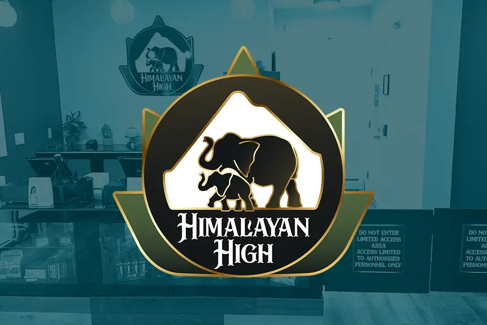A logo featuring two elephants in front of a mountain, with the text "Himalayan High" below. Silhouettes are in a circular emblem with triangular accents. Background shows an interior space.