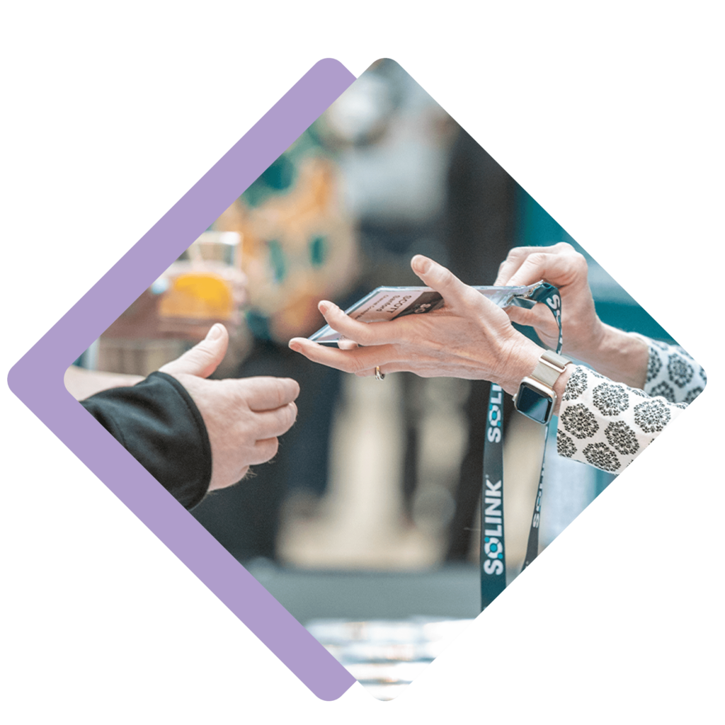 Two people exchange a name badge and lanyard at an event registration table, with one person wearing a smartwatch.