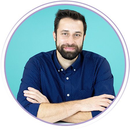 A man with dark hair and a beard, wearing a navy blue shirt, sits with arms crossed and smiles in front of a teal background with a purple circular border.
