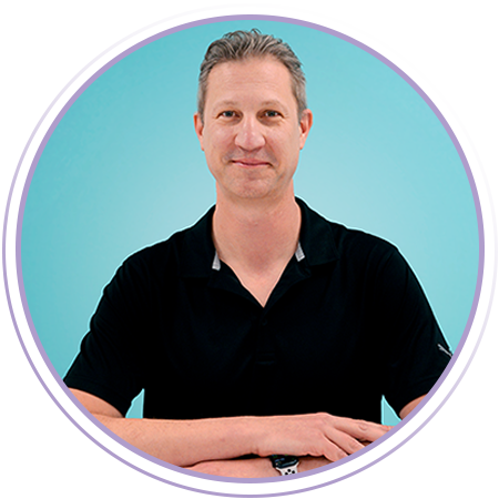 A man in a black polo shirt sits at a table with his arms crossed, in front of a turquoise background and a circular, purple graphic frame.