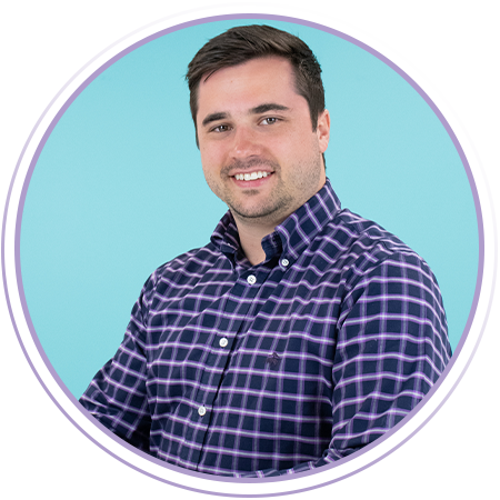 A man with short dark hair wearing a purple and navy plaid shirt sits smiling in front of a light blue background, framed by a circular purple border.