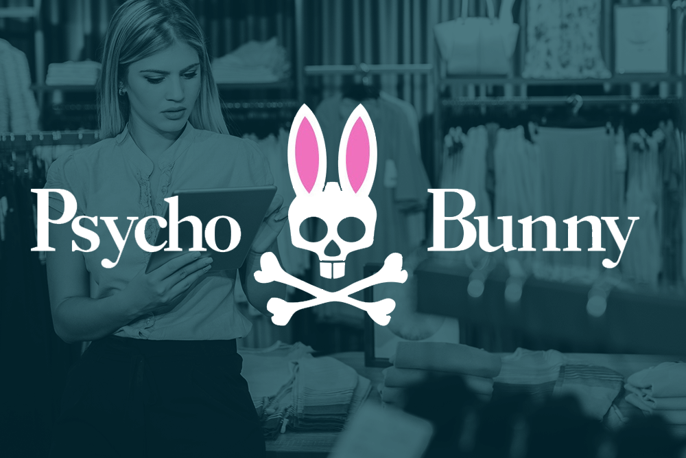 A woman looks at a tablet in a clothing store with the Psycho Bunny logo and name displayed prominently in the foreground.