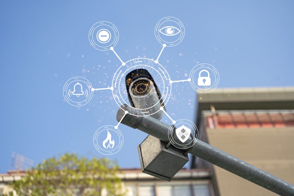 A security camera mounted outdoors with digital security icons surrounding it, representing various security features and smart technology, against a clear blue sky.