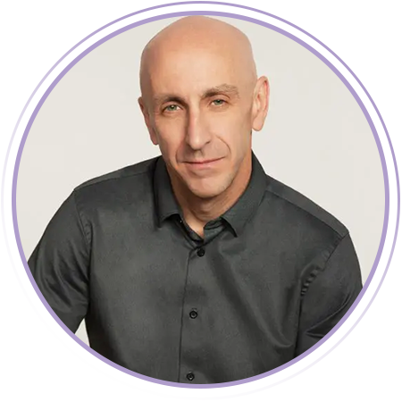 Bald man wearing a dark button-up shirt, facing forward and smiling slightly, with a neutral background.