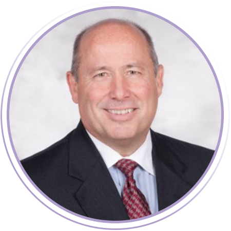 A middle-aged man in a dark suit, white shirt, and red patterned tie, smiling at the camera against a light background.