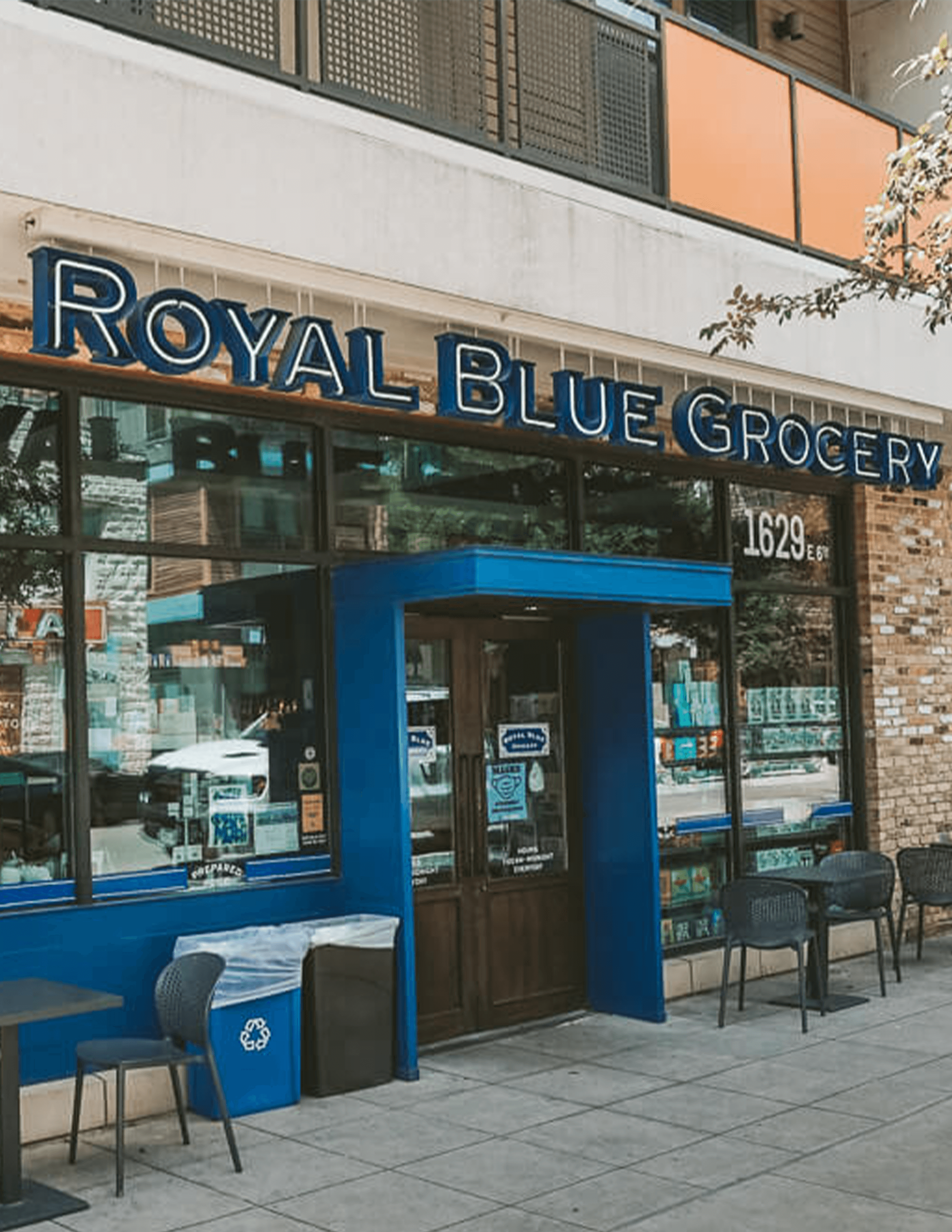 Street view of Royal Blue Grocery storefront with blue trim, glass windows, and a recycling bin on the sidewalk at 1629 East 6th Street.