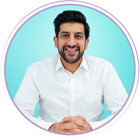 A man with dark hair and a beard, wearing a white shirt, sits with hands clasped and smiles in front of a blue background within a circular frame.