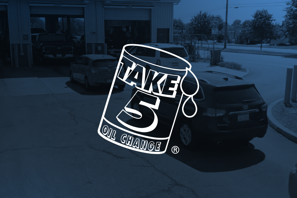 Cars are lined up outside an auto service garage with a "Take 5 Oil Change" logo overlay in the foreground.